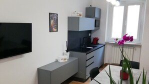 Moderni keittiö, jossa on harmaat kaapit, sisäänrakennettu mikroaaltouuni ja musta työtaso. Keittiössä on ruokapöytä tuoleineen ja ruukussa oleva viherkasvi.