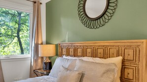 Een net opgemaakt bed met een houten hoofdbord, een bedlampje en een spiegel aan de muur.