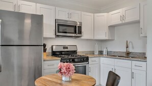 Een moderne keuken met witte kastjes, roestvrijstalen apparatuur en een houten eettafel met een bloevas.