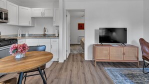 Een moderne keuken met witte kasten, een houten eettafel en een flatscreen televisie op een houten kast.