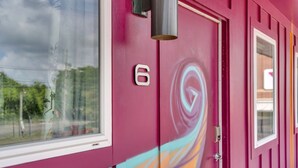 Een gebouw met een roze gevel, een raam en een deur met het nummer 6.
