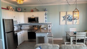 A modern kitchen with white cabinets, stainless steel appliances, and a dining area with a table and chairs. - Oceanfront - The Ocean Club - Sand, Sun & Family Fun - Indian Beach/Emerald Isle (Indian Beach)