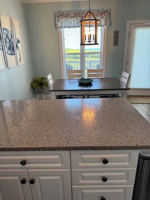 A kitchen with a granite countertop, white cabinetry, and a hanging light fixture.