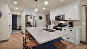 A modern kitchen with white cabinets, stainless steel appliances, a large island with stools, pendant lighting, and a clock on the wall. - 4 bedroom - 3 bath bike to downtown Sister Bay, Door County. (Sister Bay)