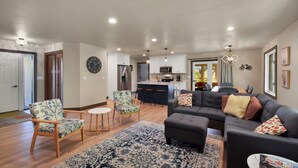 A spacious living room with a grey sectional sofa, patterned armchairs, and a coffee table. A kitchen with white cabinets and a bar area is visible in the background. - 4 bedroom - 3 bath bike to downtown Sister Bay, Door County. (Sister Bay)