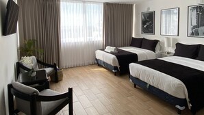 Una camera d'albergo con due letti, una scrivania, una sedia e un televisore appeso al muro.