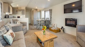 Ein modernes Wohnzimmer mit Sofa, Couchtisch, Fernseher und einer Küchenzeile im Hintergrund.