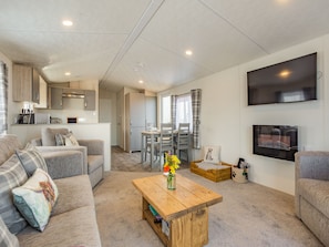 A modern living room with a sofa, coffee table, TV, and a kitchen area in the background.