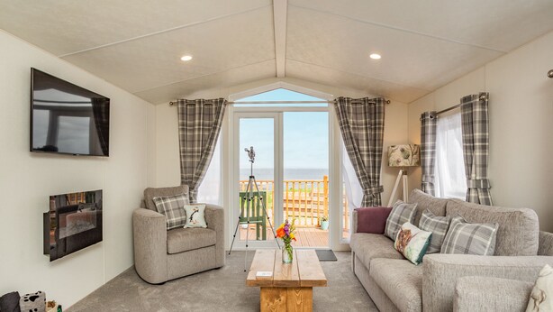 Ein Wohnzimmer mit Sofa, Sessel und Couchtisch. Ein Fernseher ist an der Wand montiert, und es gibt einen Balkon mit Blick.