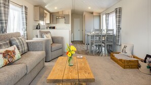 Ein modernes Wohnzimmer mit einer Couch, einem Holztisch mit Blumenvase, einem Essbereich mit Tisch und Stühlen sowie einer Küche im Hintergrund.