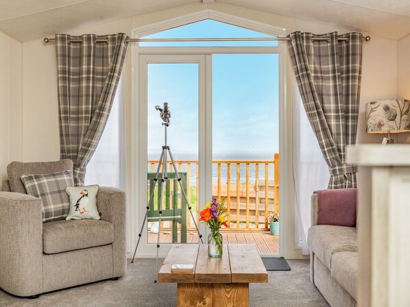 Ein Zimmer mit einer Couch, einem Tisch mit Blumenvase und Meerblick durch eine Glastür.