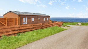 Eine Holzhütte mit geneigtem Dach, einem eingezäunten Bereich und Blick auf das Meer.