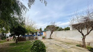 Ein Innenhof mit Betonboden, weißem Zaun und einem Baum mit Grünlaub.