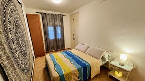 Ein Schlafzimmer mit einem Bett, Vorhängen, einem Nachttisch mit Lampe und Wandteppich.