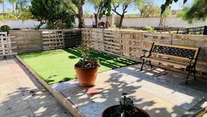 Eine Terrasse mit einer Holzbank, einem Blumentopf und einem kleinen Gartenbereich mit Kunstgrashalm.
