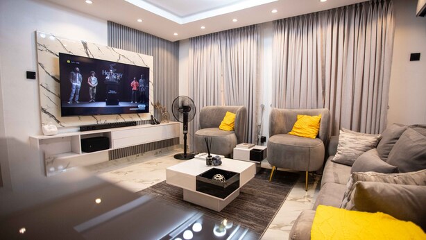 Ein modernes Wohnzimmer mit Flachbildfernseher, grauen Sofas, einem Couchtisch und einer Wand mit Marmorverkleidung.