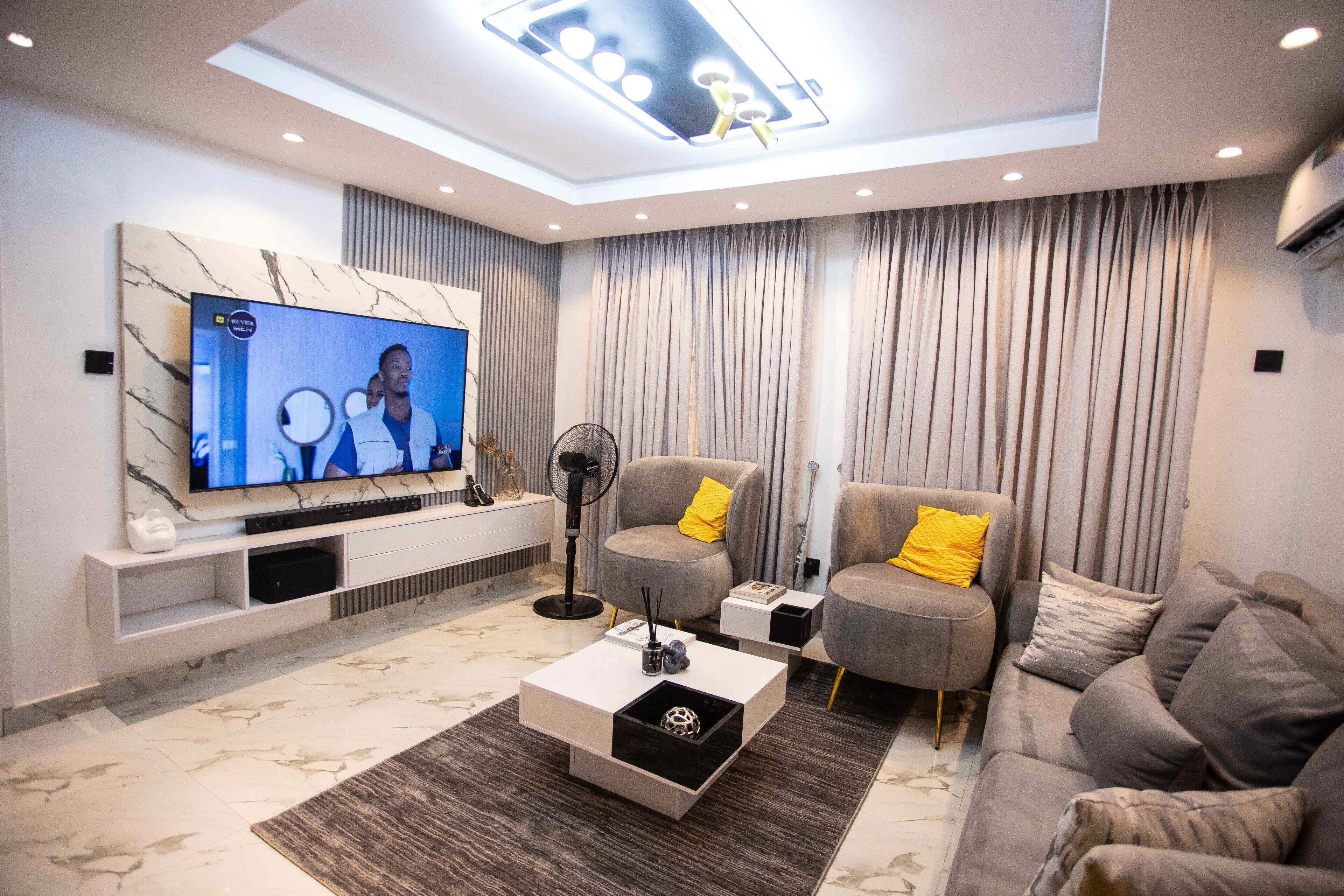 Ein modernes Wohnzimmer mit Fernseher, grauen Sofas, einem Couchtisch und einer Deckenleuchte.