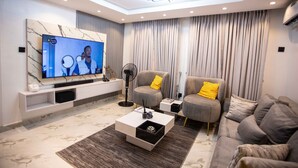 Ein modernes Wohnzimmer mit Fernseher, grauen Sofas, einem Couchtisch und einer Deckenleuchte.
