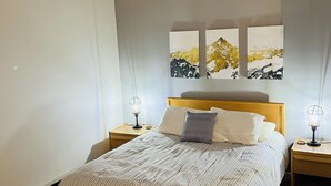 Ein ordentlich bezogenes Bett mit gestreifter Bettwäsche, zwei Nachttische mit Lampen und ein Kopfteil.