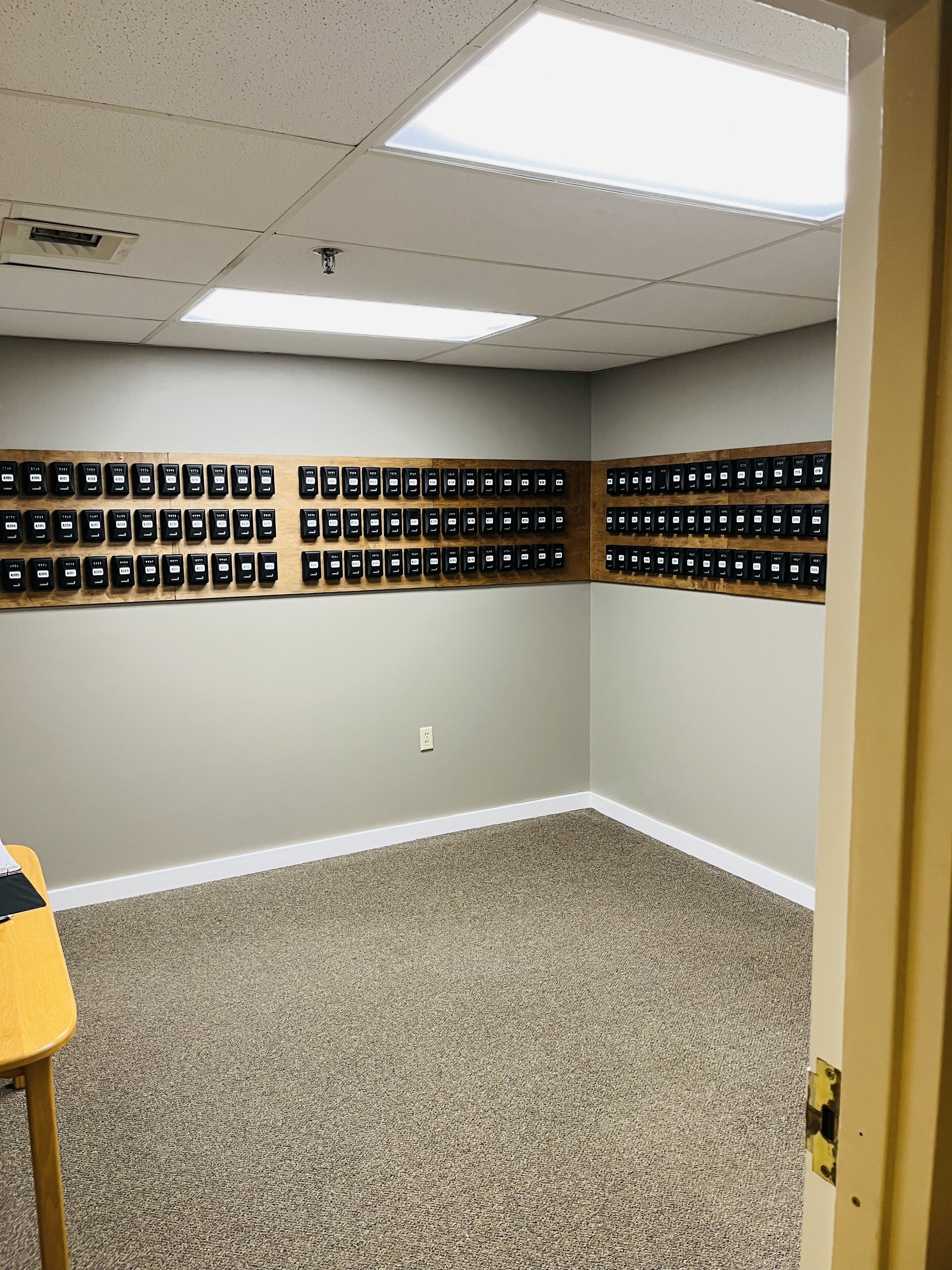 A room with carpeted flooring, a wooden table, and a wall with multiple black switches.