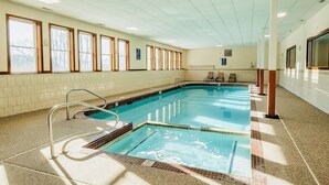 Ein Schwimmbecken mit Fliesen, einer Metallleiter und einer Fliesenwand mit Fenstern.
