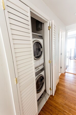 Un cuarto de lavandería con lavadora y secadora integradas, piso de madera y pared exterior blanca.