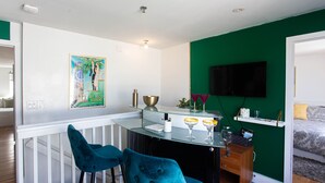 A modern kitchen with a bar area, featuring a glass countertop, two blue velvet bar stools, and a green accent wall.