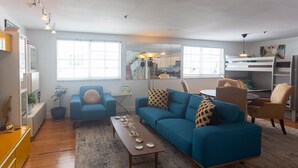 A modern living room with a blue sofa, wooden coffee table, and a dining area with a small table and chairs.