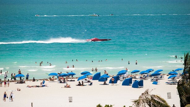 A beach with people, umbrellas, and a speedboat.