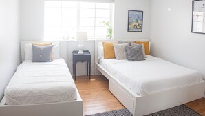 Un dormitorio con dos camas, una ventana con persianas, un ventilador de techo y una pequeña mesa con lámpara.