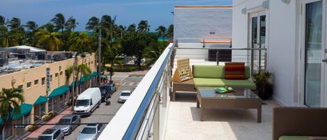 A balcony with outdoor furniture, a view of the street below, and a building with a white facade.
