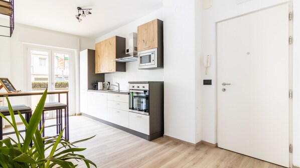 A modern kitchen with wooden cabinets, a microwave, an oven, and a coffee maker. There is a door to the right and a window to the left. - Apartment within walking distance of Merano's thermal baths and beautiful promenades (Merano)