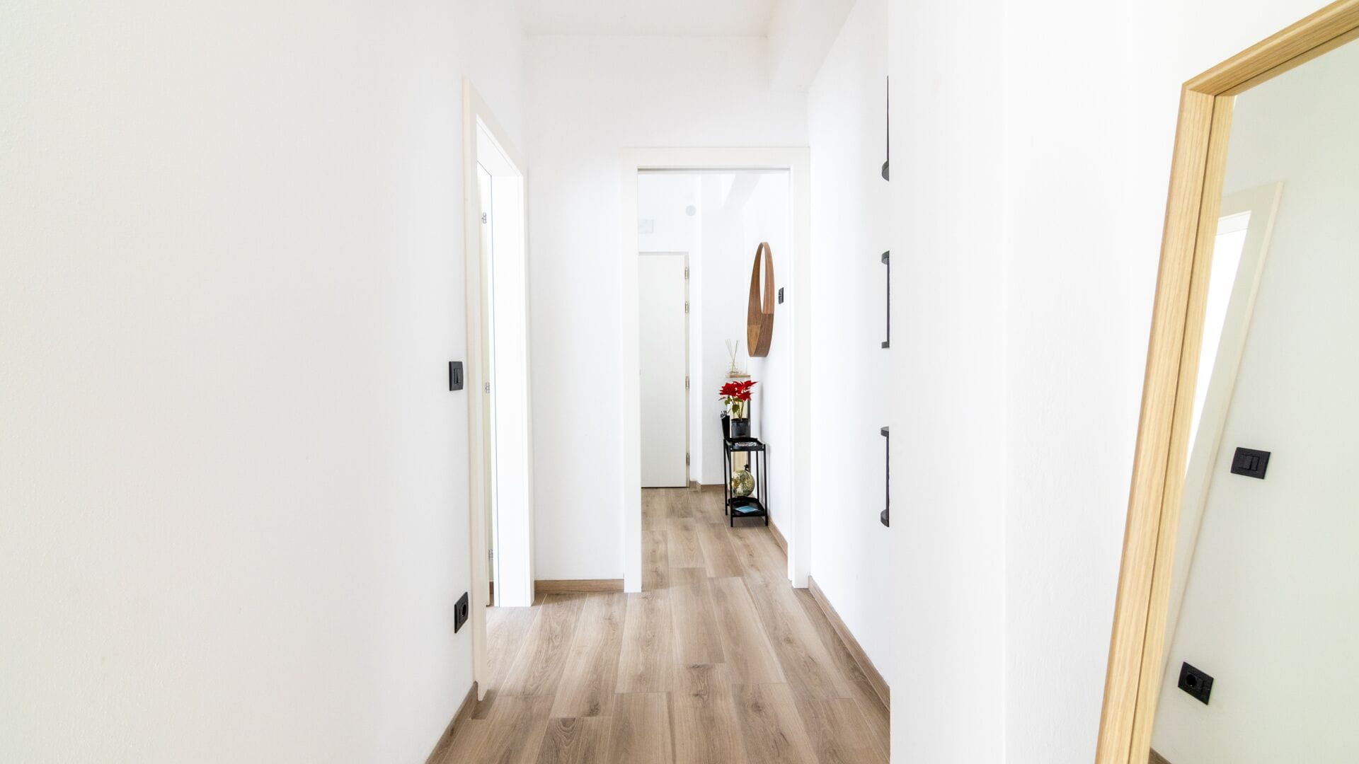 A narrow hallway with wooden flooring, white walls, and a door at the end.