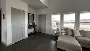 A spacious living room with a large sectional sofa, a fireplace, and a view of the outdoors through large windows. - Contemporary all new, entire home perfect for a luxury getaway (Fort Davis)