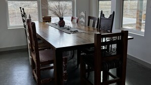 A dining room with a large wooden table, six chairs, a chandelier, and large windows with a view of the outdoors. - Contemporary all new, entire home perfect for a luxury getaway (Fort Davis)