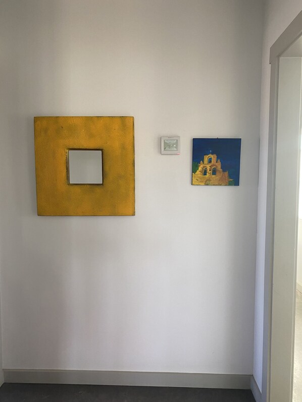 A room with a textured wall panel, a thermostat, and a painting of a building.
