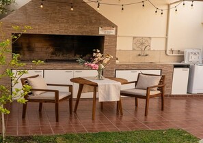 An outdoor dining area with a brick fireplace, a table with chairs, and a sign above the fireplace. - Premium home for up to 7 guests with a private garage (Mendoza)