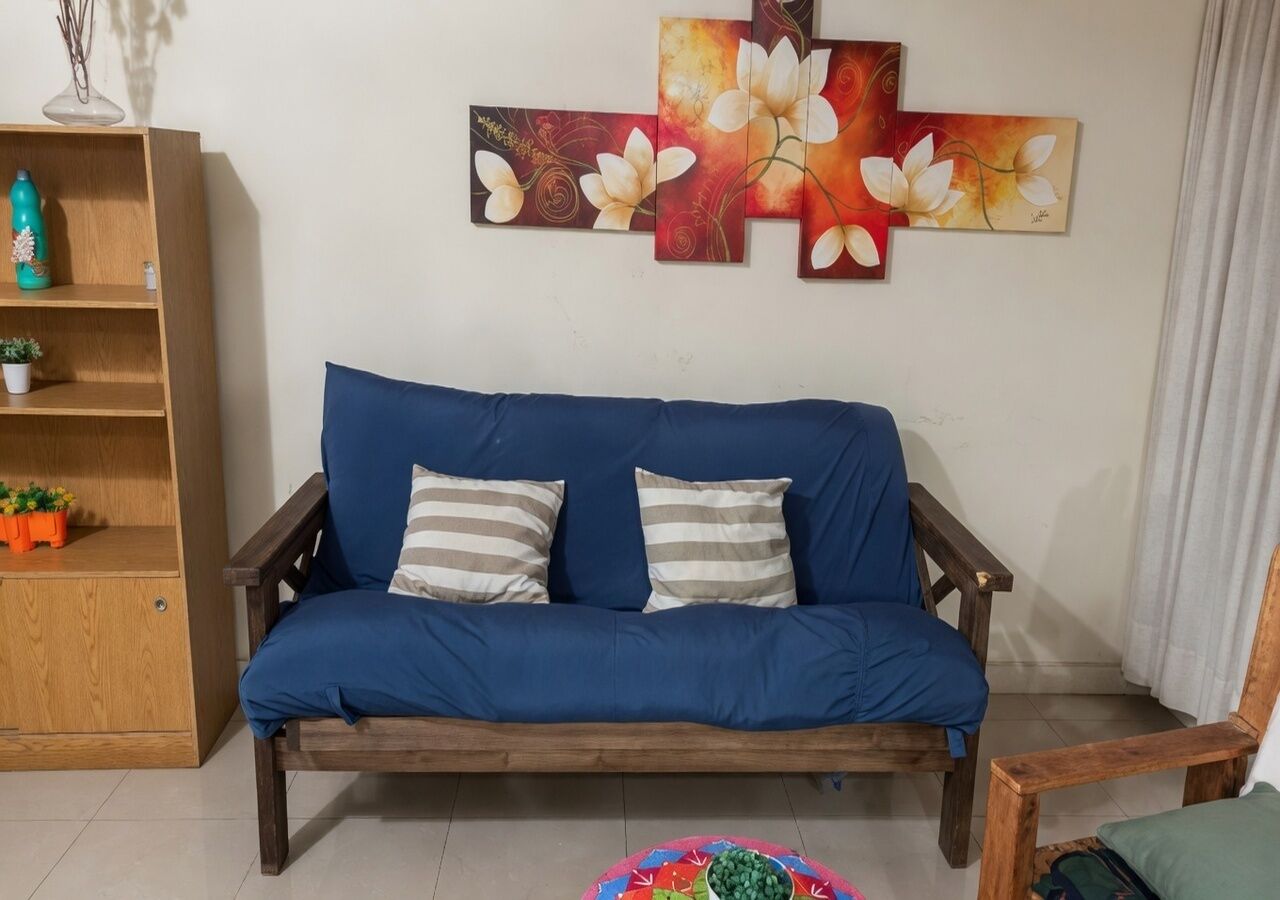 Ein blaues Sofa mit gestreiften Kissen, ein Holztischchen mit einer Pflanze und eine Wand mit einem floralen Gemälde.