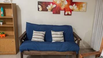 Ein blaues Sofa mit gestreiften Kissen, ein Holztischchen mit einer Pflanze und eine Wand mit einem floralen Gemälde.