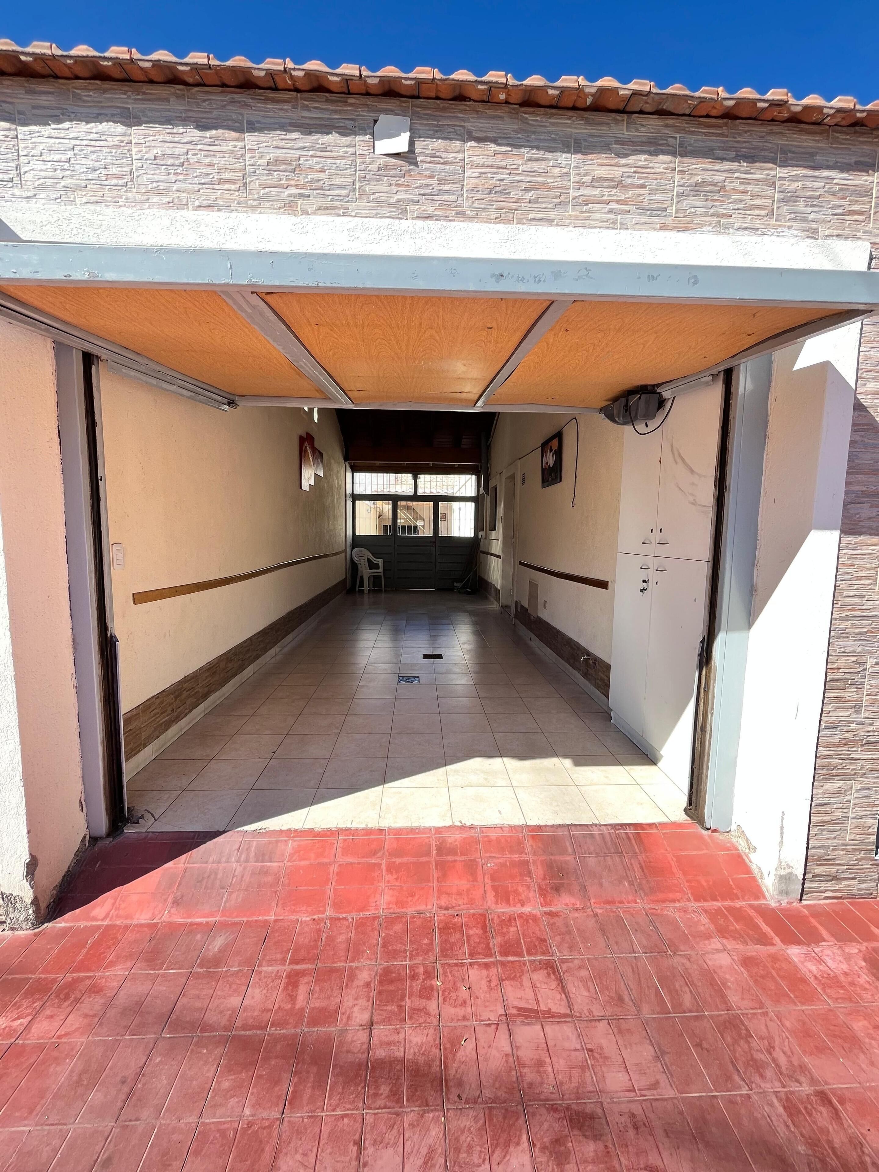A covered outdoor corridor with a tiled floor, a wooden ceiling, and a view into a building with a tiled roof.