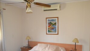 Ein Schlafzimmer mit einem Bett, zwei Nachttischen, einem Deckenventilator, einer Klimaanlage und einem gerahmten Gemälde an der Wand.
