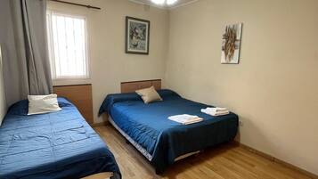 A room with two single beds, a ceiling fan, a window with curtains, and a wooden floor.