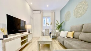 Una sala de estar moderna con un televisor de pantalla plana, una mesa de centro de madera, un sofá gris y una zona de comedor con una mesa y sillas blancas.