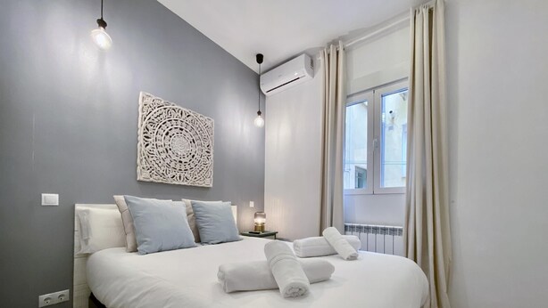 Un dormitorio moderno con una cama grande, un adorno en la pared, un equipo de aire acondicionado y una ventana con cortinas.