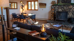 A cozy living room with a fireplace, a dining area, and a sign indicating the location is in the White Mountain National Forest. - Modern Mountain Chalet Near Storyland & Summer Fun (Intervale)