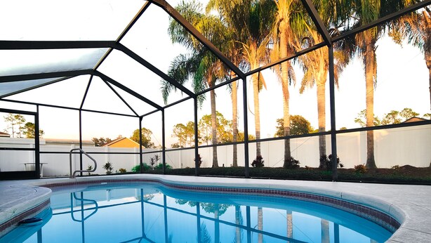 A swimming pool with a clear blue water surface, surrounded by a metal fence and palm trees. - Tropical Paradise - Private Heated Pool, Screened Lanai, No Cleaning Fee (Lakeland)