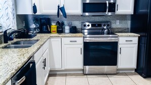A modern kitchen with white cabinets, stainless steel appliances, and a granite countertop. - Tropical Paradise - Private Heated Pool, Screened Lanai, No Cleaning Fee (Lakeland)