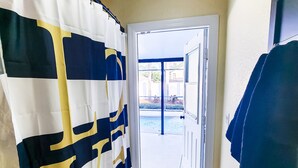 A bathroom with a shower curtain featuring a geometric pattern, a towel rack, and a view of a pool through an open door. - Tropical Paradise - Private Heated Pool, Screened Lanai, No Cleaning Fee (Lakeland)