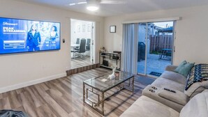A modern living room with a flat-screen TV, a glass coffee table, a sofa, and a sliding glass door leading to a patio. - So Flo Getaway, * Close to beach! * (Fort Lauderdale)