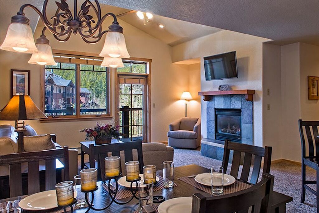 A dining area with a fireplace, a television mounted above it, and a window with a view of a house.